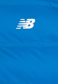 Plava sportska tkanina s istaknutim bijelim "NB" logotipom. Glatka tekstura s minimalnim naborima, pogodna za sportsku odjeću.