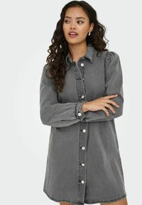 Robe chemise en denim gris avec des manches longues, fermeture par boutons à l'avant et légèrement bouffantes aux épaules. Elle présente un ourlet arrondi et des accents de boutons en argent.