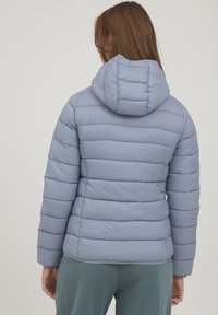 Doudoune bleu clair avec capuche, présentant des lignes de quilting horizontales, une texture douce et une coupe ajustée. La vue de dos montre le volume et la silhouette.