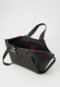 Black leather tote bag with a textured finish, silver hardware, and a zip closure. Interior features a red branded pocket and minimalist design.