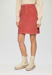 Jupe A-line en velours côtelé rouge avec une taille ceinturée et des poches devant, associée à des bottines beiges à cheville avec une semelle épaisse.
