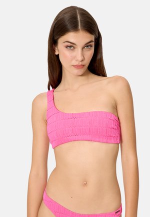 Mujer joven con cabello largo y castaño, vestida con un bikini texturizado de un solo hombro en color rosa brillante y parte inferior a juego, sobre un fondo liso.