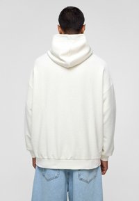 Witte oversized hoodie met een zachte textuur, grote capuchon en geribbelde manchetten. G gedragen met lichtblauwe denim shorts.