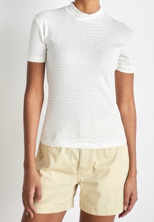 Bílé tričko s krátkým rukávem s žebrovanou texturou a opakovaným potiskem loga "Calvin Klein Jeans". Doplněno světle béžovými šortkami.