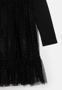 Svart kjole med lange ermer, tettsittende liv og en gathered tulle skjørt dekorert med små, runde paljetter.