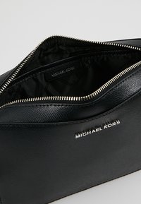 Pochette zip in pelle nera texturizzata di Michael Kors con lettering in logo argentato e fodera interna in tessuto nero.