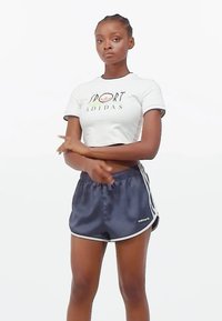 Kratka bijela majica s natpisom "SPORT" i logom, u kombinaciji s mornarskim satenskim sportskim kratkim hlačama koje imaju bijele bočne pruge i mali akcent s logom.