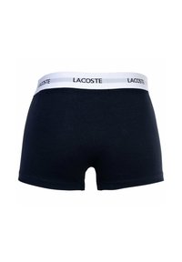 Navy blue boxer shorts made of cotton with a white elastic waistband featuring the logo "LACOSTE" in black lettering.