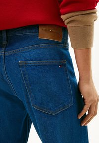 Granatowe dżinsy z denimu z brązową skórzaną łatą z nadrukiem "TOMMY HILFIGER", pomarańczowymi szwami i tylną kieszenią z małym logo.