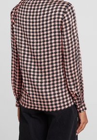 Blus med långa ärmar i svart och rosa hundtandsmönster, mjukt tyg, rundad nederkant och plisserad axeldetalj.