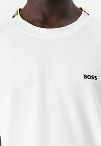 T-shirt en coton blanc avec un tissu texturé, un col rond et un logo "BOSS" noir. Accentuée par une bande multicolore au col.