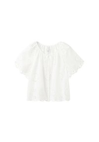 Blouse blanche à manches courtes avec motifs floraux en ajourage, bords festonnés et fermeture à nouer sur le devant, présentée sur un fond uni.