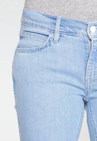 Jeans de mezclilla azul claro con un corte ajustado, que presentan un diseño de cinco bolsillos y cierre de botón clásico con un solo botón en la parte superior.