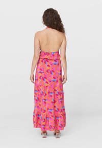 Robe maxi avec un col halter, présentant un motif floral vibrant en rose, orange et bleu. Ceinture volantée et ourlet en couches.