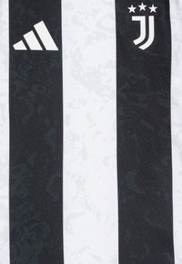 La camiseta a rayas en blanco y negro presenta un logo de Adidas en blanco a la izquierda, con un emblema de la Juventus a la derecha, todo con un patrón texturizado.