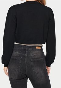 Svart kort tröja med långa ärmar, rund halsringning och ribbat kant. Kombinerad med mörkgrå jeans med bakfickor och etikett.