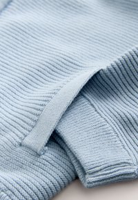 Tissu tricoté côtelé bleu clair plié pour montrer la texture et les bords avec un gros plan sur le détail de la manche et de la couture latérale.