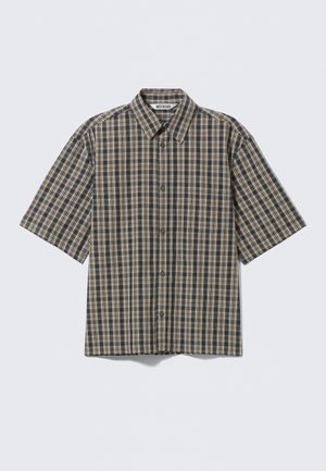 Chemise à manches courtes avec boutons, motif à carreaux beige, noir et bleu, et une poche poitrine avant, posée à plat sur un fond clair.