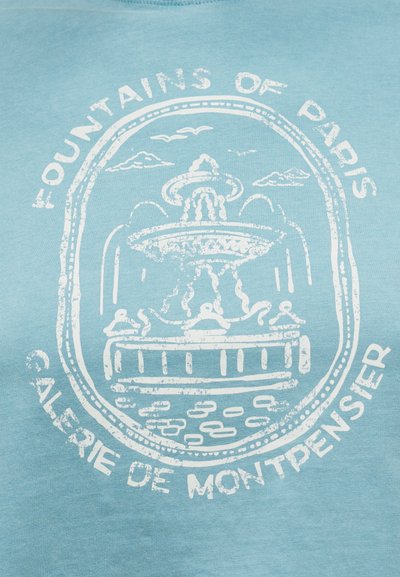 Σχέδιο λευκού vintage συντριβανιού με πουλιά και σύννεφα, περικυκλωμένο από το κείμενο "Συντριβάνια του Παρισιού" και "Galerie de Montpensier" σε μπλε ύφασμα.