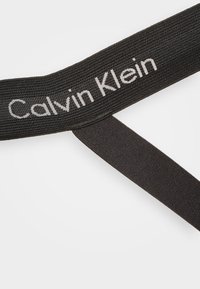 Schwarzes elastisches Band mit dem "Calvin Klein"-Logo in Weiß, das eine strukturierte Oberfläche und eine klare, rechteckige Form aufweist.