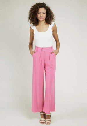 Pantalons larges roses avec des plis et une taille haute, dotée de deux boutons, associés à un débardeur blanc ajusté.