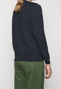 Felpa navy con scollo a girocollo e polsini a costine, abbinata a pantaloni verdi. Tessuto liscio con cuciture minime e senza marchi visibili.
