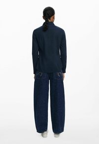 Navyblaues Langarmshirt mit strukturierten Wellenmustern, kombiniert mit weit geschnittenen blauen Jeans mit Sprenkeln und dekorativer Naht.