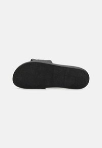 Black sandal sole with a textured surface, featuring a slightly raised edge and a smooth, rounded toe. Minimalistic design, flat profile.