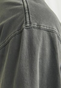 Grå bomuldsstof med synlige syninger, der fremviser en glat tekstur og et afslappet design. Fokus på skuldersøm og stofdråbe.