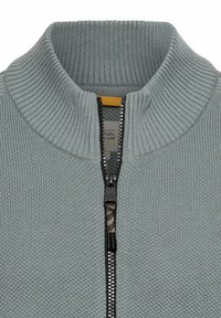 Lichtgrijze cardigan met ritssluiting, geribde kraag en een getextureerd breipatroon. Voorzien van een zwarte rits met een oranje trekker.