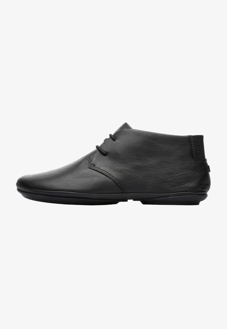 Chaussure décontractée noire en cuir montant à la cheville avec coutures minimales, deux œillets pour les lacets, et une fine semelle noire vue de profil.