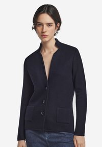 Granatowy kardigan z teksturowanym splotem, z kołnierzem szalowym, przednimi kieszeniami i trzema dużymi guzikami wzdłuż zapięcia.