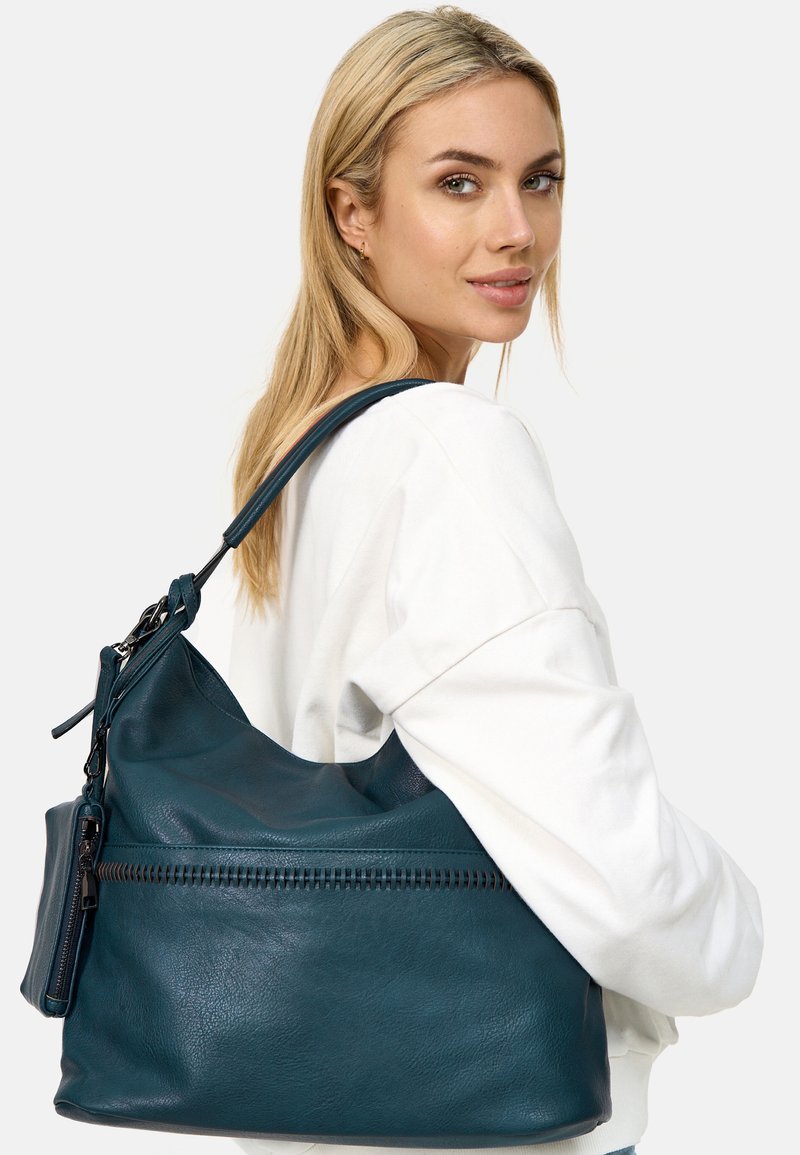 Teal leren handtas met een slouchy ontwerp, voorzien van een ritsvak en een gestructureerde afwerking, gedragen op de schouder met een lange schouderband.