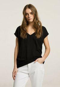 Czarny t-shirt z dekoltem w serek, krótki rękaw, luźny krój, wykonany z miękkiego materiału, w połączeniu z białymi spodniami. Prosty fason, bez widocznych wzorów czy akcentów.