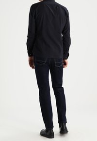 Camisa oscura de manga larga con cuello, combinada con vaqueros oscuros de ajuste entallado y botines negros; detalles de costuras visibles en los vaqueros.