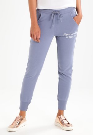 Person wearing light blue jogger pants with drawstring waist and white "Abercrombie & Fitch" logo on left thigh, paired with metallic rose gold sneakers.