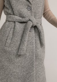 Grau gemusterte Weste aus Wollmischung mit einer weichen Textur, ausgestattet mit einem gebundenen Taillengurt, zwei Fronttaschen und Knopfverschlüssen.