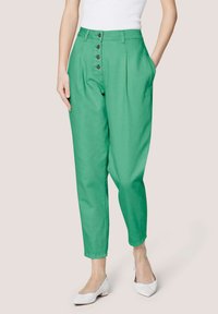 Grüne hoch-taillierte Hose mit Knopfverschluss, seitlichen Taschen und schmal zulaufendem Bein. Aus einem glatten Stoff gefertigt. Mit grauen Knöpfen akzentuiert.