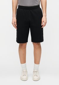 Juodi medvilniniai šortai su elastine juosmens juosta, kelių ilgio, su kontrastingo rašto šoninėmis juostelėmis. Dėvimi su baltais batais ir kojinėmis.