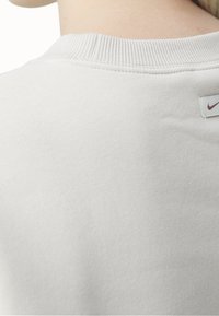 Light gray, cotton athletic sweatshirt with a ribbed crew neck and a small Nike logo tag on the back, featuring a smooth texture.