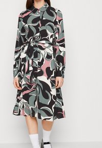 Vzorované šaty z hladké tkaniny s kombinací zelených, růžových, černých a bílých vírů, s límcem, knoflíky a svázaným pasem.