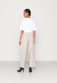 Vit kortärmad skjorta med avslappnad passform, kombinerad med beige vida byxor och svarta högklackade skor; mjukt tyg och elastisk midja.