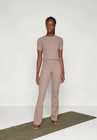 Tan aktiivne rõivaste komplekt, mis sisaldab lühikeste varrukatega pluusi ja laienevaid legginsid. Kanga pind tundub sile ning disain on kehakujuga ja minimaalsete õmblustega.