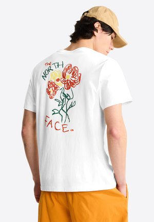 Young person wearing beige cap, white T-shirt with red, yellow floral sketch and "The North Face" text on back, paired with orange shorts.