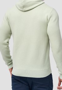 Sudadera con capucha verde claro de acabado texturizado, con puños y dobladillo acanalados, y un corte holgado. La parte posterior es lisa, sin detalles visibles.