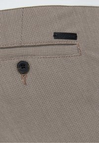 Brun texturerad tyg av byxor med en bakficka som har en svart etikett och en svart knapp nära det övre sömmen.