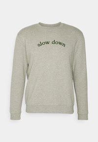 Felpa grigia chiara realizzata in misto cotone con polsini e orlo a costine. Presenta la scritta verde "slow down" arcuata sul davanti. Design minimalista.