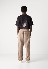 Black t-shirt with a pink graphic on the back, paired with loose-fitting beige cargo pants and off-white sneakers.