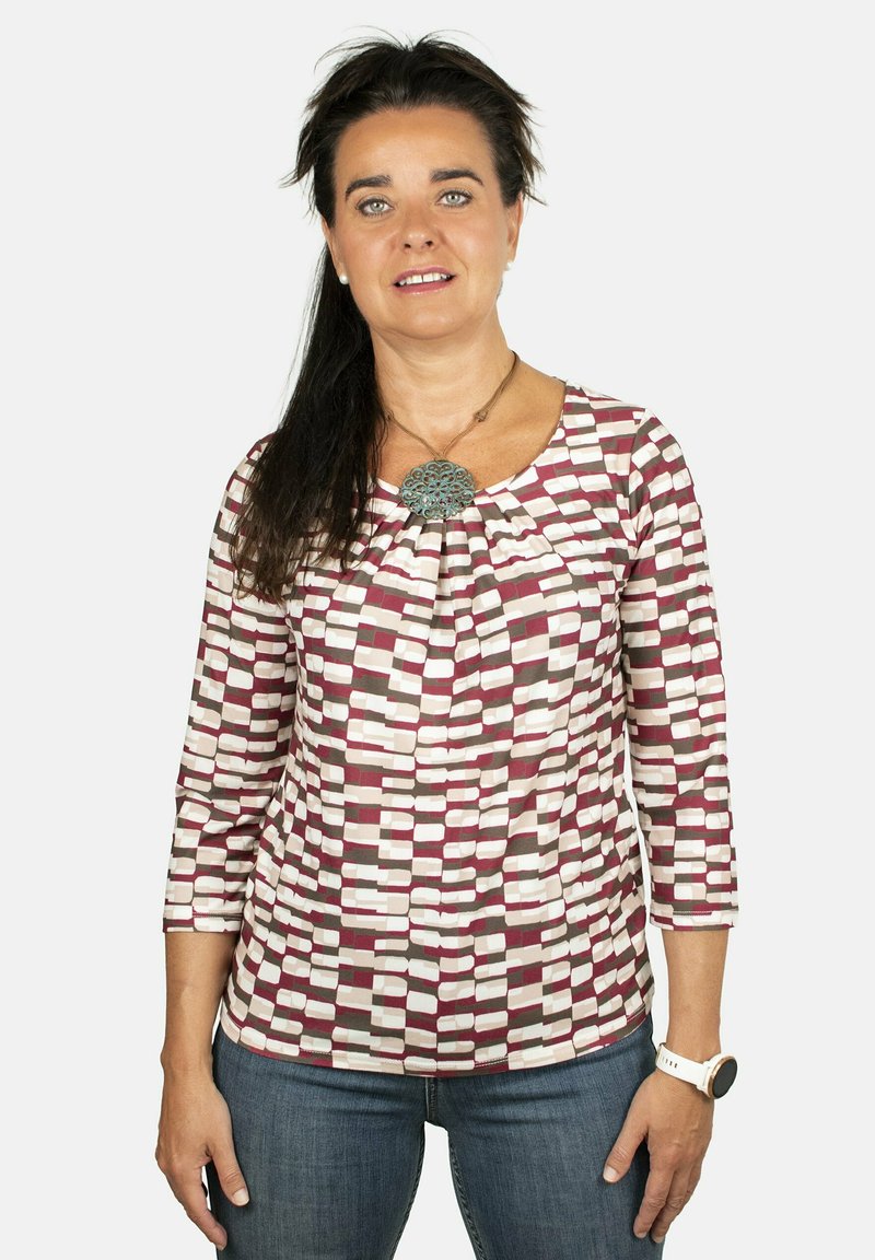 Top de manga larga con un patrón geométrico en burdeos, rosa y beige sobre un fondo claro. Cuello redondo con detalle de fruncido.