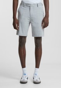 Shorts de cuadros grises con frente plano, bolsillos laterales y cierre de botón. Llevados con calcetas deportivas blancas y zapatillas multicolores.